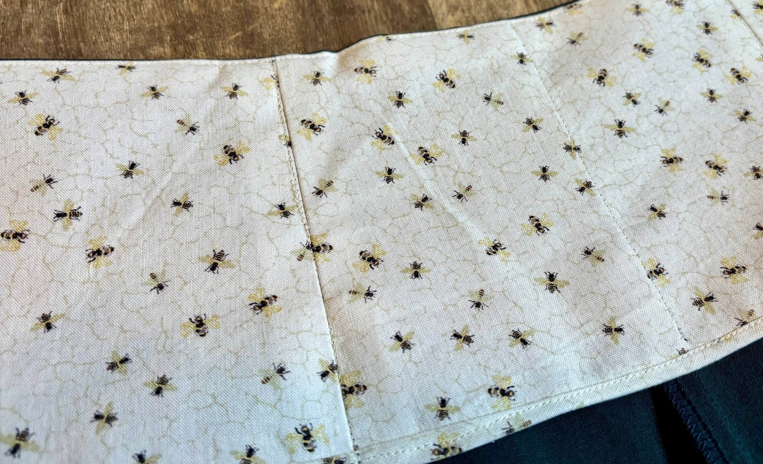 a detail shot of some panels of quilting cotton with bees flying on a cream background, showing a bias bound seam over the main fabric of the interior of the shorts.