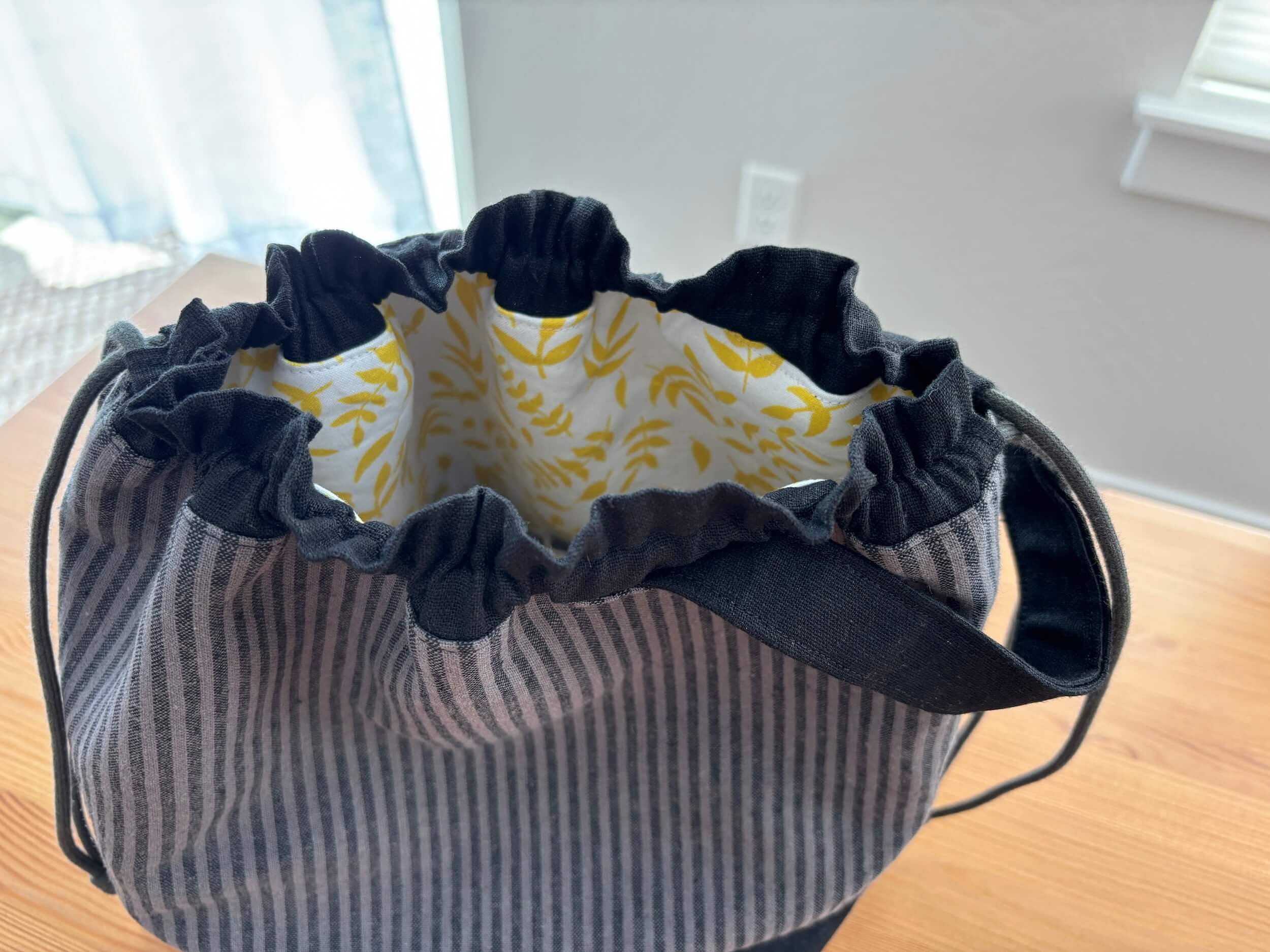 A detail of a bag where you can see inside the bag and see a yellow leaf design with a draw string around the top.